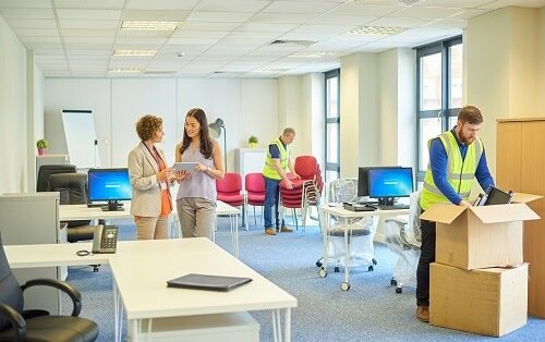 Professional moving team packing office electronics, computer monitors, and chairs during a commercial office relocation service.