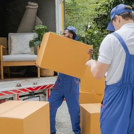 Professional movers wearing blue uniforms loading large cardboard boxes into a moving container for efficient house shifting.