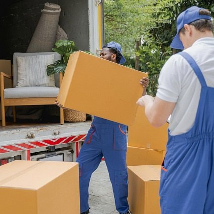 Professional relocation team in blue overalls carrying large cardboard boxes toward an open moving truck